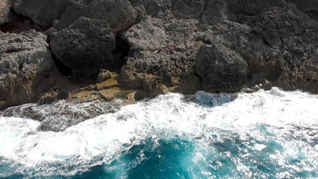 Reversal drone shot of a young man and woman sitting on a limestone cliff overlooking the beautiful blue ocean