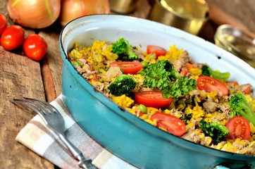 Close-up of tuna risotto with vegetables, tomatoes, broccoli and parsley in the old pan, onions, cans and oil in the background