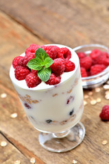 Close-up of greek yoghurt with oatmeal and fresh raspberries in a glass and mint leaves - vertical photo