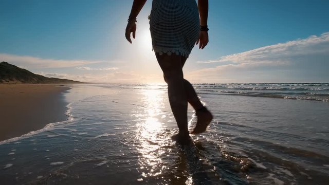 Slow motion shot of womans torso relaxed walk in shallow water along the sand beach at Pardoe Northdown Conservation Area Tasmania with open ocean and sunset on the background