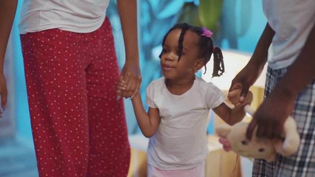 Beautiful young african family dancing together at home. Cute portrait of little black girl with braids holding parents hands.
