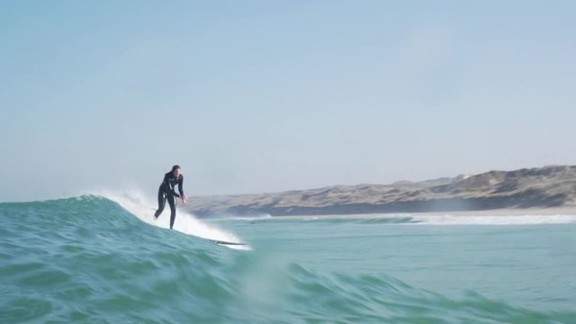 In water shot of a surfer girl popping up onto her longboard and then riding a wave out over the spray into the golden light