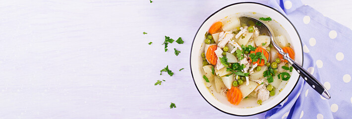 Chicken soup with green peas, carrots and potatoes in a white bowl on a light background. Banner....