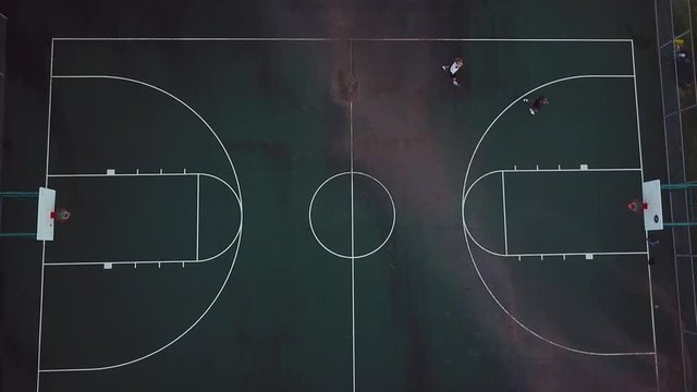Drone Shot directly above a local, outdoor basketball court where two men are playing each other. In this shot, one man shoots a three-pointer and makes it.