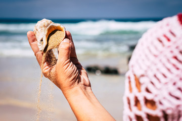 Nature and environment concept with close up of woman hands with shell and sand - travel and holiday summer vacation at the beach - blue sea and waves in background