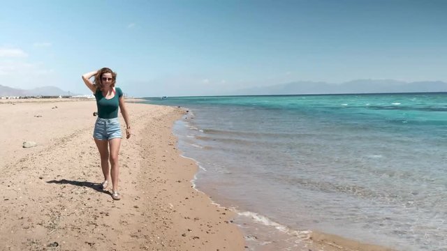 Beautiful clear water in Dahab Egypt. Exploring the blue water with mountains in the background and people windsurfing and kite surfing. Lady walking on the beach