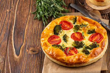 Vegetable pie with broccoli, peas, thyme. tomatoes and cheese on wooden background. Copy space.