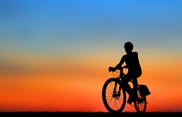 Plakat Silhouette man and bike relaxing on blurry sunrise sky background.