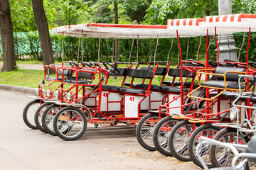 Fototapeta na wymiar Red cyclo velomobiles with a canopy for the whole family. Parked rental tourist trike vehicles. Ecological transport for walking and sports.
