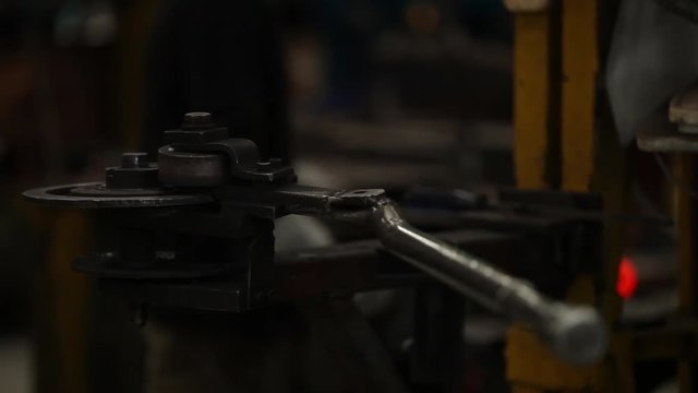 Close up of an idle metal bending machine with a worker hammering a metal bar in the background.