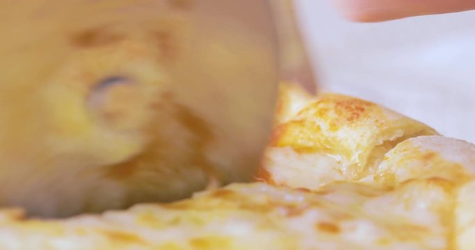 Taglio pizza margherita italiana con rotella di metallo su un tagliere di legno.