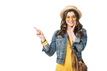 front view of smiling boho girl in denim jacket pointing with finger isolated on white