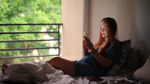 lifestyle woman in the bedroom with the phone lying in bed.