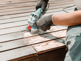 Male hands polishing dark wooden plank with angle grinder and metal brush