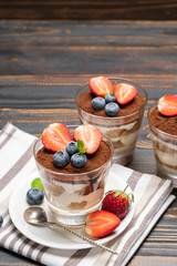 Classic tiramisu dessert with blueberries and strawberries in a glass on wooden background