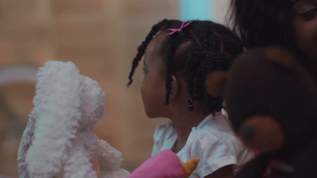 Close-up of beauty adorable african child with barids holding soft toys and playing at home.