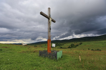 Fototapeta na wymiar KYIV, UKRAINE - MAY 19, 2017: Wooden cross stands in the field, around the mountain and runs a white horse