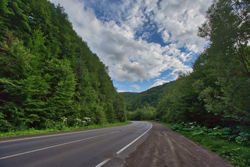 Fototapeta premium The road to the mountains. Poor quality asphalt pits and green trees