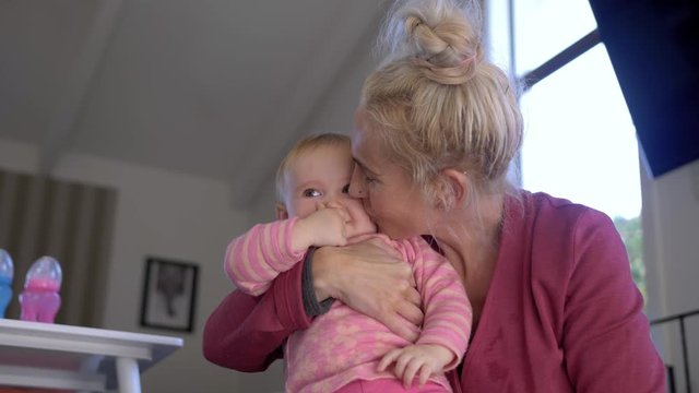A blonde haired woman kisses a baby on the cheek as she laughs and claps her hands