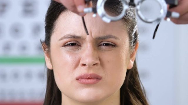 Woman with partly closed eyes, doctor putting phoropter on patients face, vision