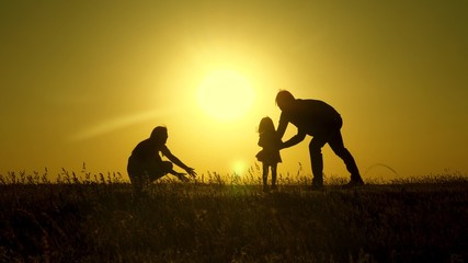 Fototapeta na wymiar parents play with their little daughter. mother and Dad play with their daughter in sun. happy baby goes from dad to mom. young family in field with a child 1 year. family happiness concept.