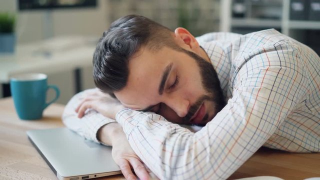Close-up of handsome young businessman sleeping in office lying on laptop on desk relaxing resting. Break at work, tired youth and heavy overwork concept.