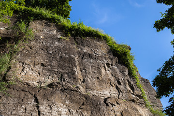 A stone rock is covered with grass on the background of a virtually cloudless sky.