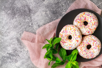 American sweetness glazed donuts and fresh mint on a gray surface against a background of pink fabric close up top view