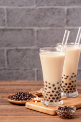 Popular Taiwan drink - Bubble milk tea with tapioca pearl ball in drinking glass and straw, wooden table gray brick background, close up, copy space