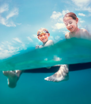 Sister and brother sitting on inflatable mattress and enjoying the sea water, cheerfully laughing when swim in the sea. Careless childhood vacation time unusually unerwater camera shot image.