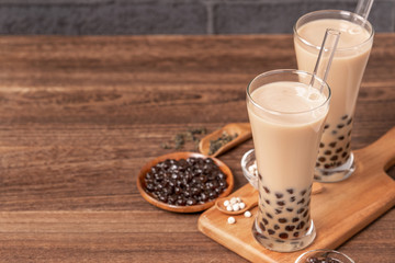 Popular Taiwan drink - Bubble milk tea with tapioca pearl ball in drinking glass and straw, wooden table gray brick background, close up, copy space