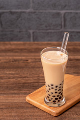 Popular Taiwan drink - Bubble milk tea with tapioca pearl ball in drinking glass and straw, wooden table gray brick background, close up, copy space