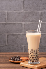 Popular Taiwan drink - Bubble milk tea with tapioca pearl ball in drinking glass and straw, wooden table gray brick background, close up, copy space
