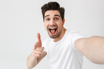 Excited happy young man posing isolated over white wall background make a selfie by camera.