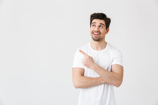 Excited young man posing isolated over white wall background pointing.