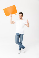 Emotional excited young man posing isolated over white wall background holding speech bubble.