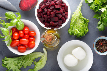 Ingredients for summer salad (tomatoes, basil, lettuce, soft cheese, olive oil and spices) on the table.