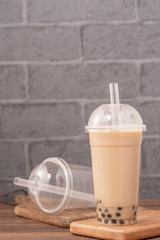 Takeout with disposable item concept popular Taiwan drink bubble milk tea with plastic cup and straw on wooden table background, close up, copy space