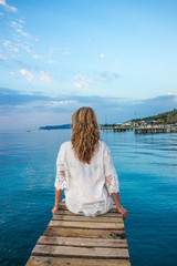 The girl is sitting on the pier alone.
