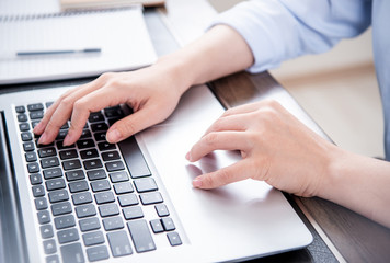 Business concept. Woman in blue shirt typing on computer with coffee on office table, backlighting, sun glare effect, close up, side view, copy space