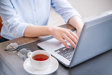 Business concept. Woman in blue shirt typing on computer with coffee on office table, backlighting, sun glare effect, close up, side view, copy space
