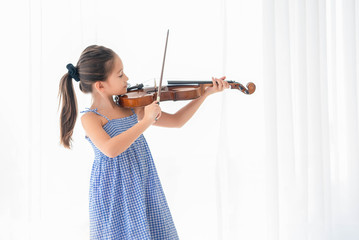 Cute girl playing violin in white bedroom with white curtain background. Musical and people lifestyles. Education and recreation concept. Back to school theme