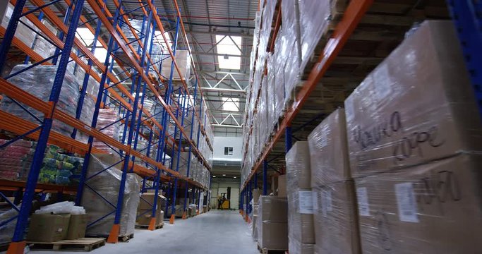 Camera moves between shelves with palettes and boxes in a big modern logistic warehouse. Shot on 6K RED camera.