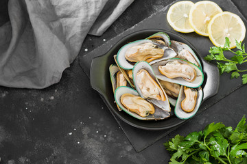 Raw kiwi mussels in a black plate on a dark background