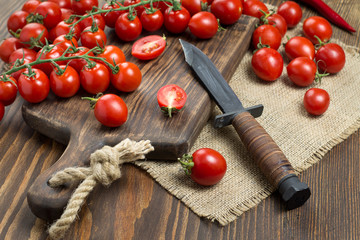 The small red cherry tomatoes are scattered on a wooden table with an old knife