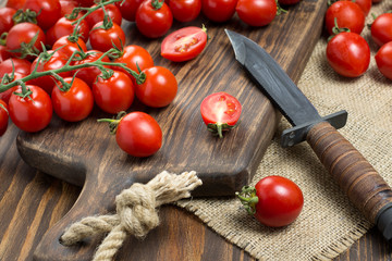 The small red cherry tomatoes are scattered on a wooden table with an old knife