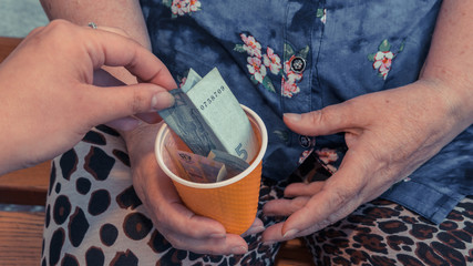 Old woman begs for alms. Closeup of money and coins in hand of poor woman.