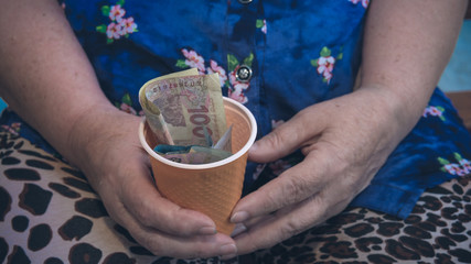 Old woman begs for alms. Closeup of money and coins in hand of poor woman.
