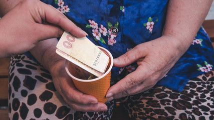 Old woman begs for alms. Closeup of money and coins in hand of poor woman.