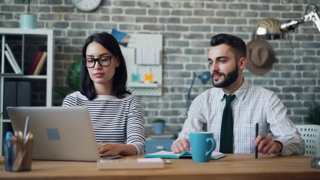 Cinemagraph loop of office worker playing with pen working with laptop in workplace together with attractive girl. People, cooperation and technology concept.